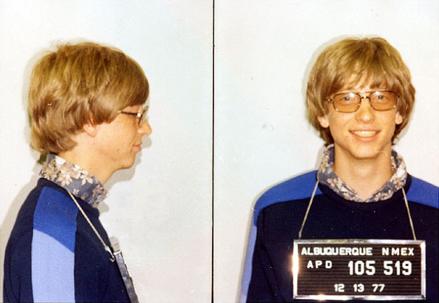 Bill Gates in a 1977 police mugshot, smiling, with a height chart behind him